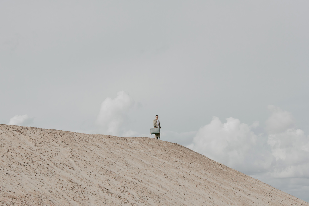 Man Standing on a Desert Land Holding a Luggage 